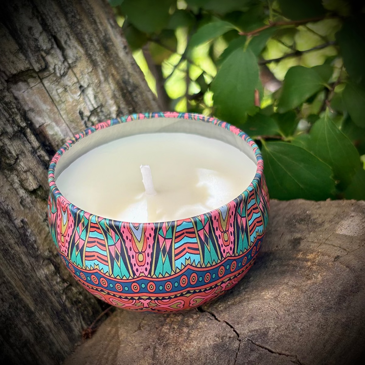 Decorative candle in a colorful holder on a stone surface with greenery in the background