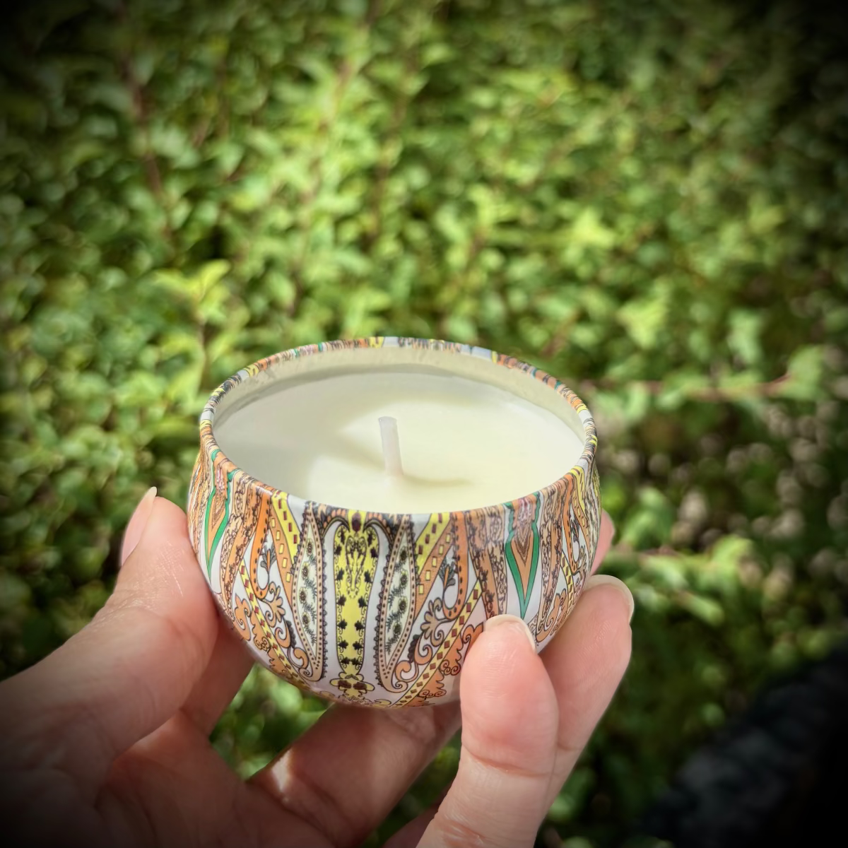 Hand holding a patterned candle against a green outdoor background