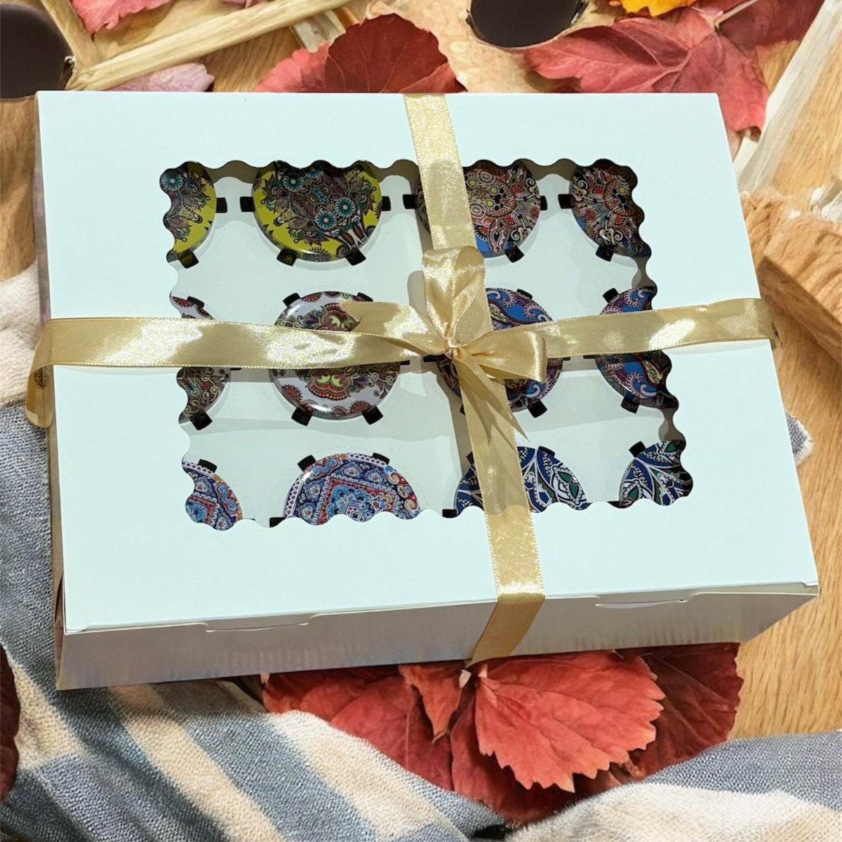 Gift box with decorative items inside, tied with a ribbon, on a wooden surface with autumn leaves.