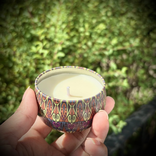 Hand holding a small candle with a colorful container against a green outdoor background