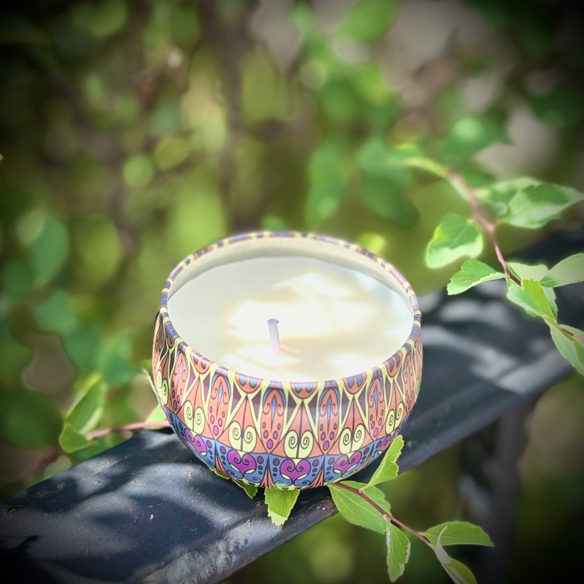 Decorative candle in a colorful holder on a branch with green leaves in the background