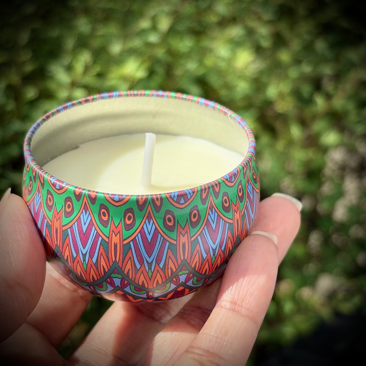 Hand holding a colorful patterned candle against a natural background