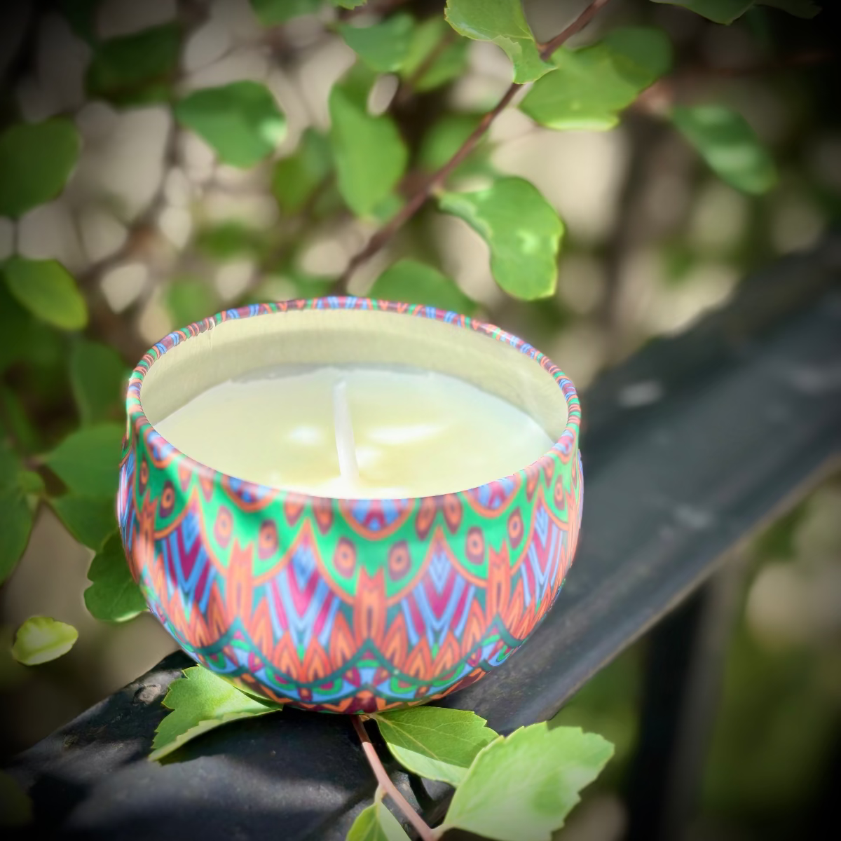 Colorful patterned candle holder with a candle inside, placed on a branch with green leaves.