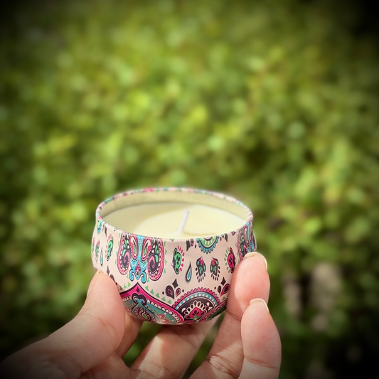 Hand holding a small candle with a colorful paisley design against a blurred green background