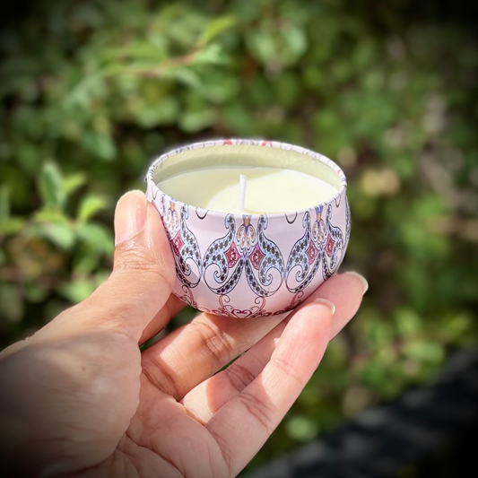 Hand holding a small patterned candle holder with a candle inside against a blurred green background