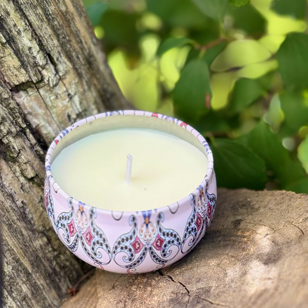 Decorative candle in a patterned holder on a wooden surface with greenery in the background