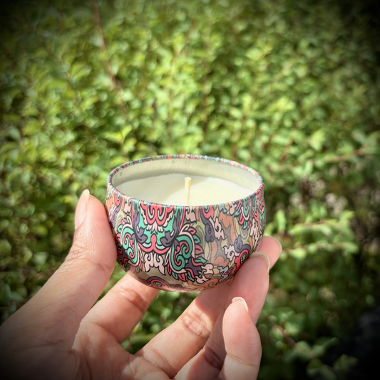 Hand holding a small candle with a colorful pattern against a green outdoor background
