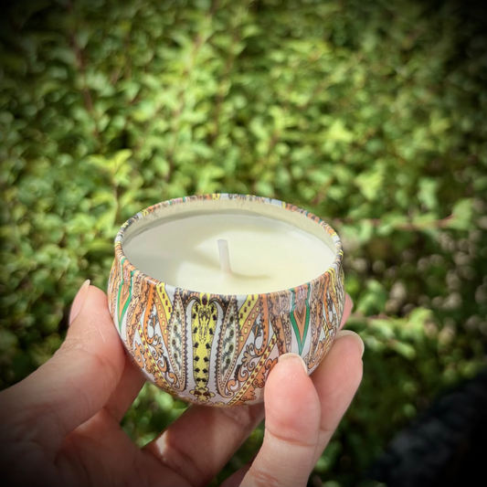 Hand holding a patterned candle against a green outdoor background