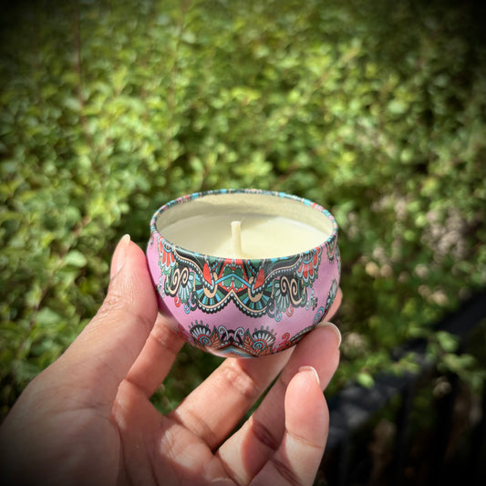Hand holding a small candle with a colorful design against a green outdoor background